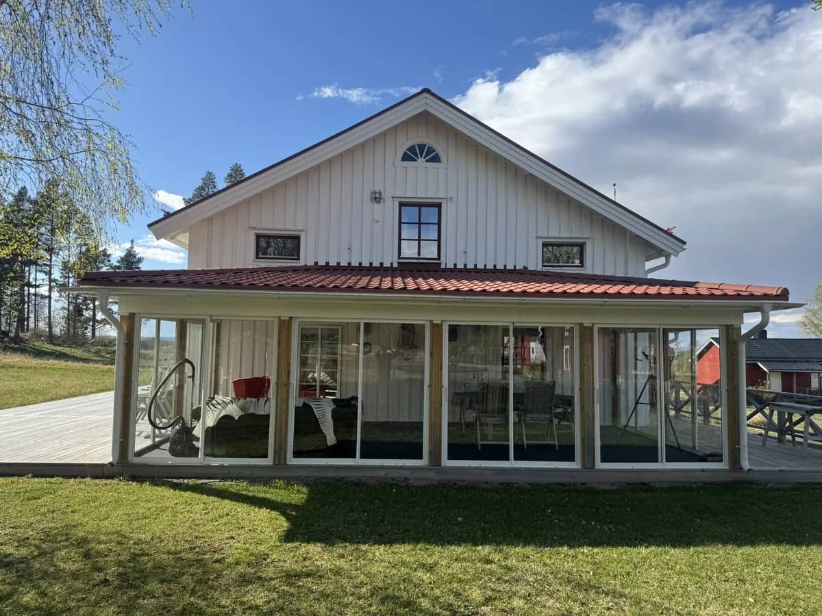 Vitt trähus med rött tak och inglasad veranda